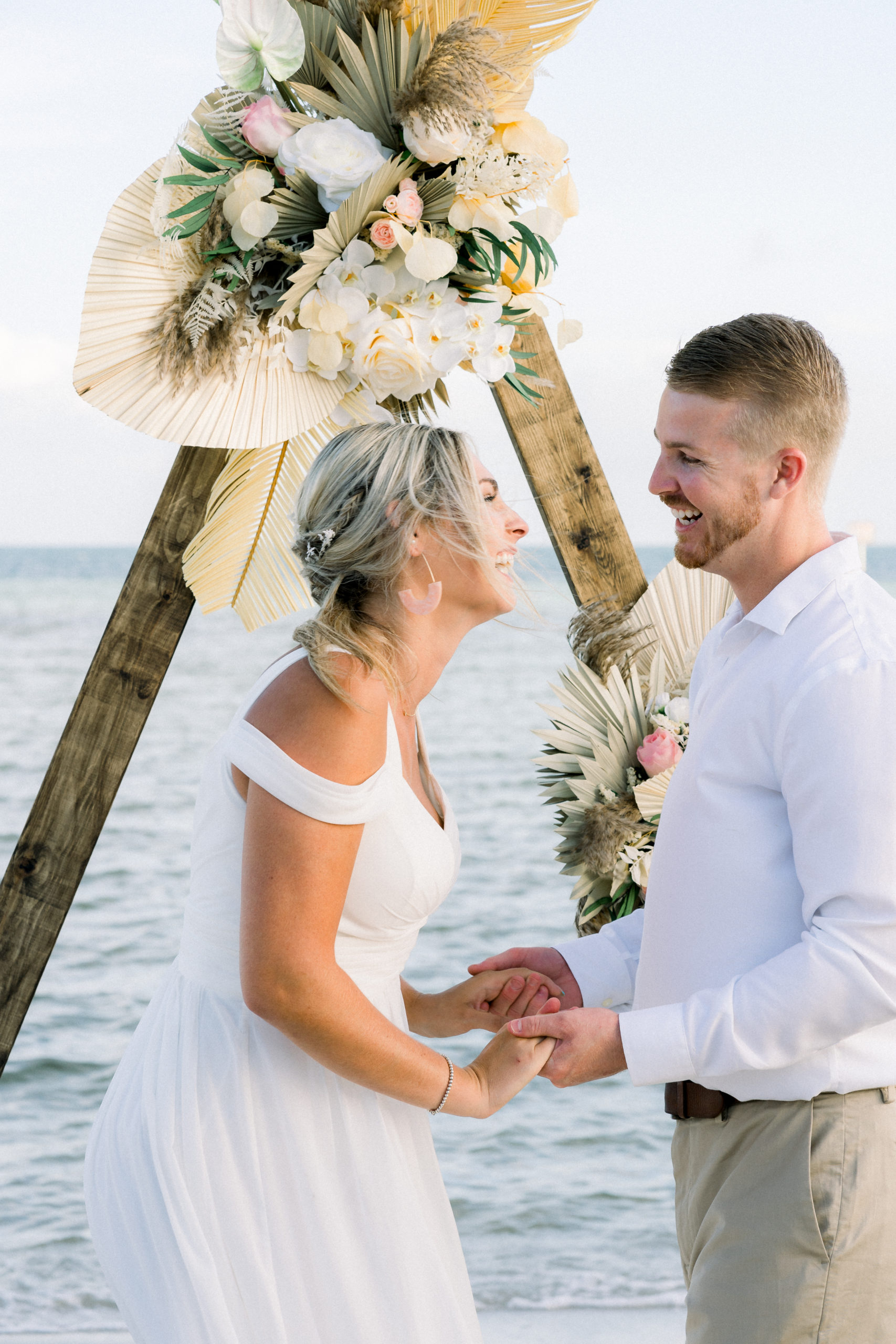 A couple having an intimate beach elopement ceremony, smiling at each other.
