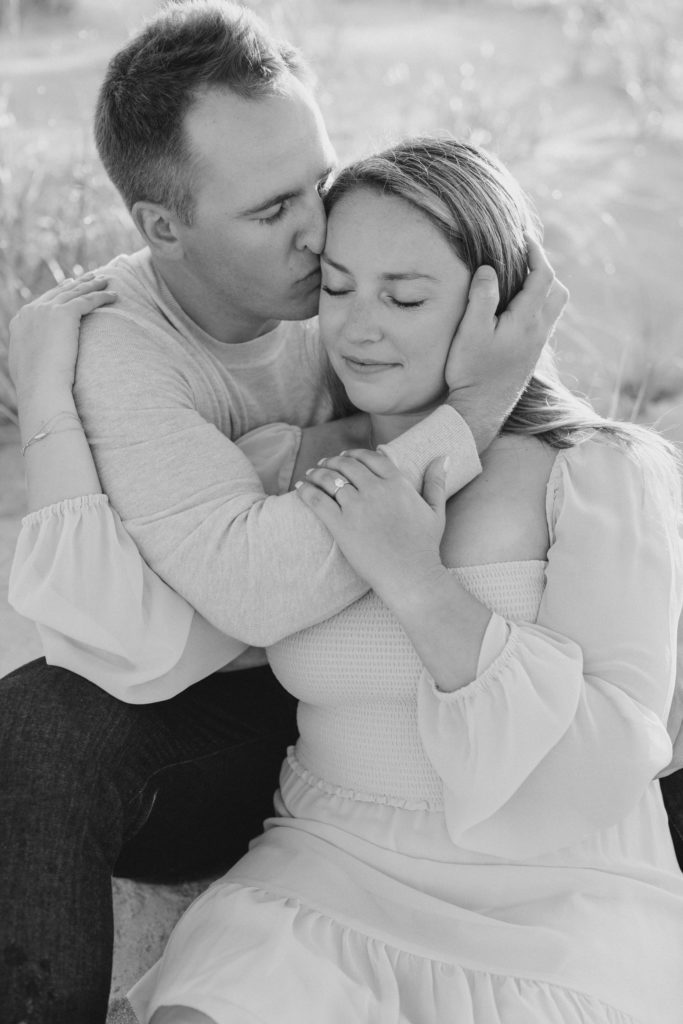 Couple cuddling on Cape May beach at sunrise during engagement session