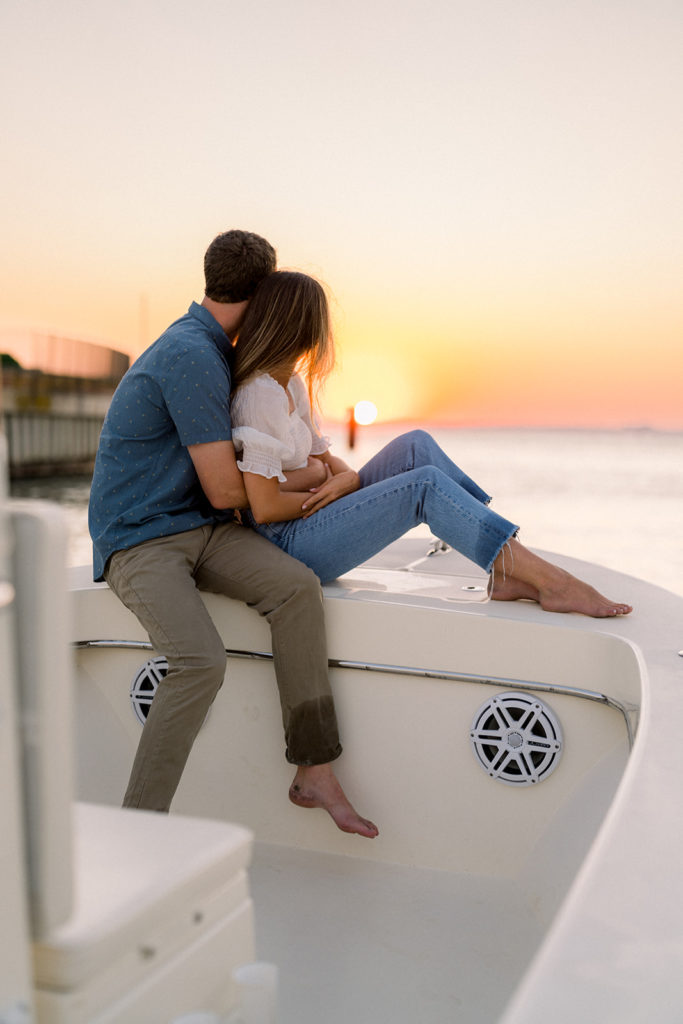 Couple sitting on boat during engagement session and watching the sunset