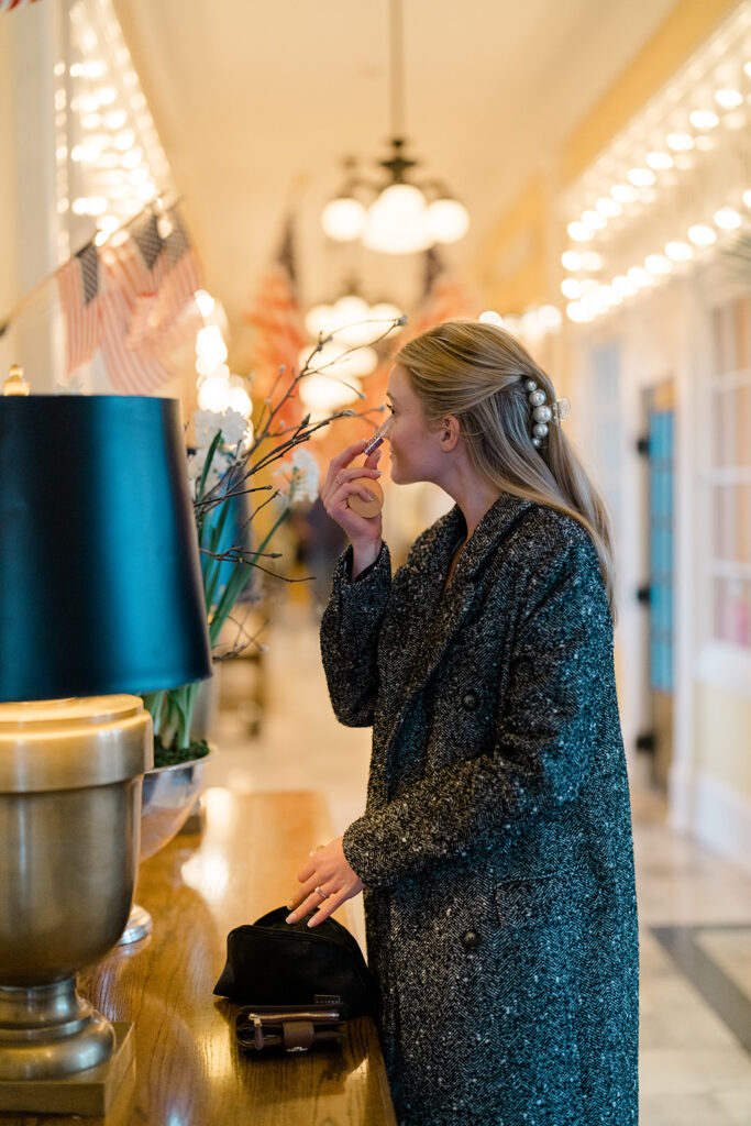 Woman puts on makeup in mirror of the lobby of Congress Hall in Cape May, New Jersey for her charming engagement session