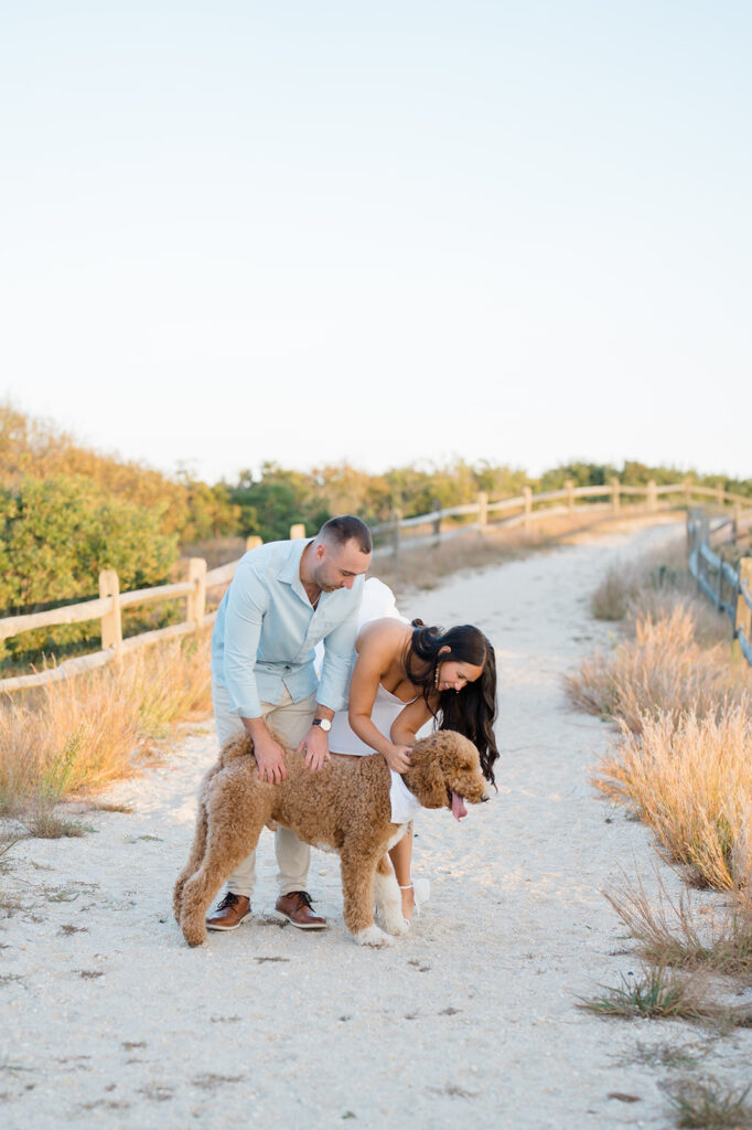 Couple petting their dog on the beach during engagement session photos in Avalon, New Jersey